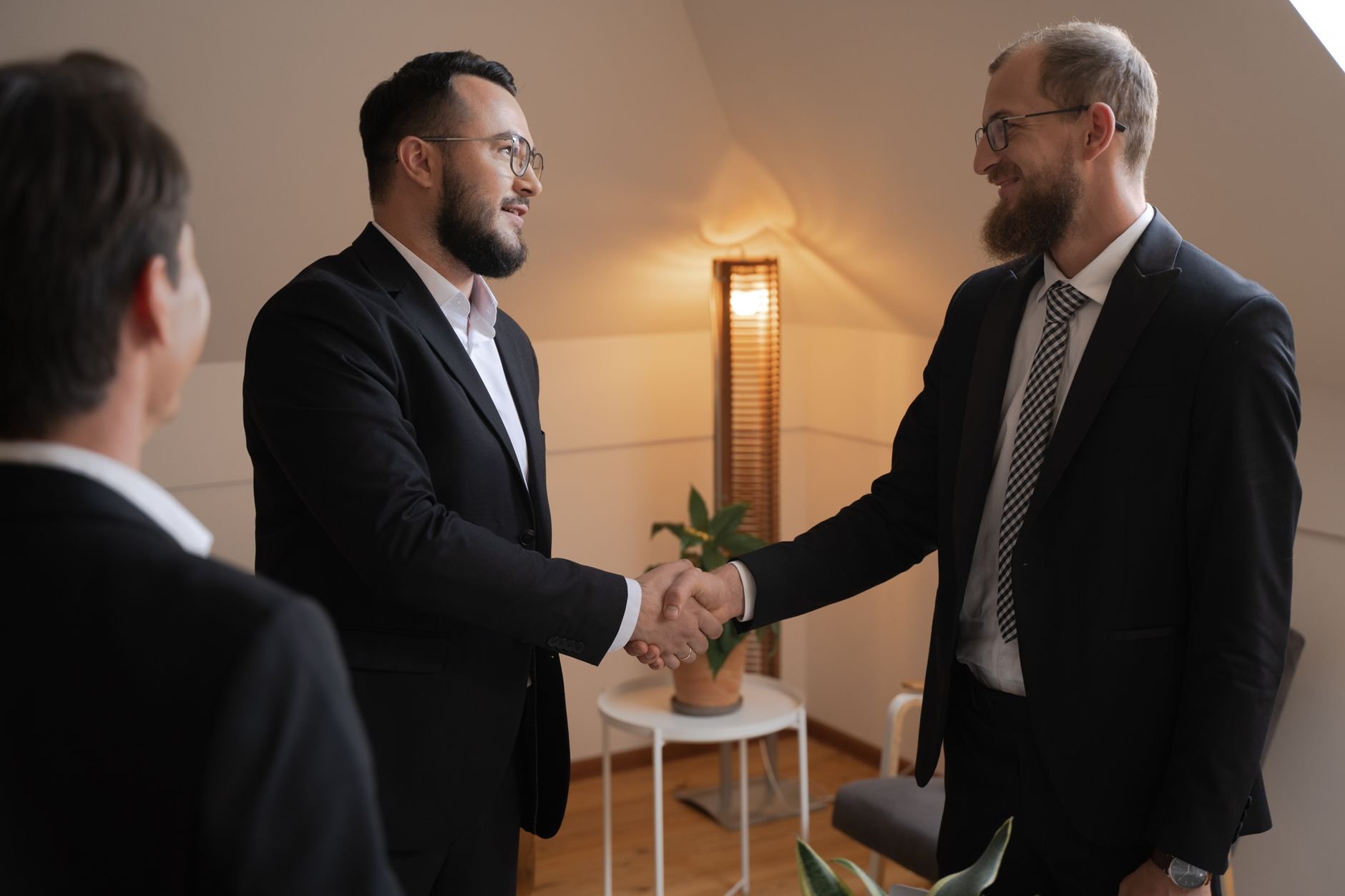 Two businessmen shaking hands in a warm office setting — a deal done with care