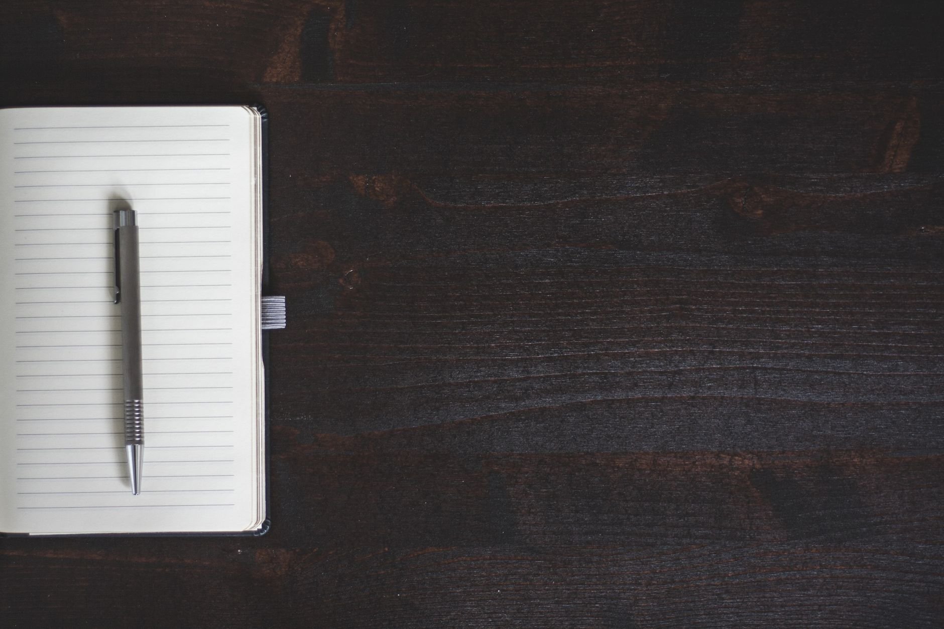 Open notebook and pen on a dark wooden desk — the workspace of a deliberate operator